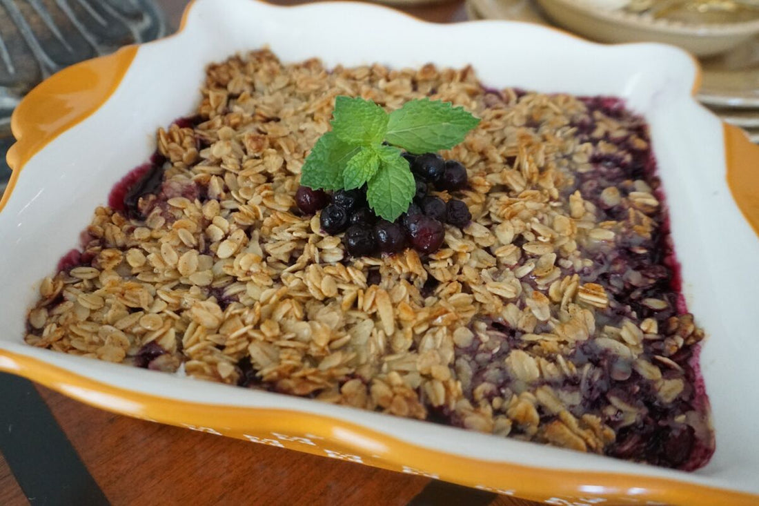 GoodShoog™ Berry Crisp with golden oat topping and blueberry filling in a white baking dish, garnished with fresh mint